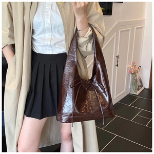 Detail of dark brown tote bag featuring glossy patent leather and a bow tie accent