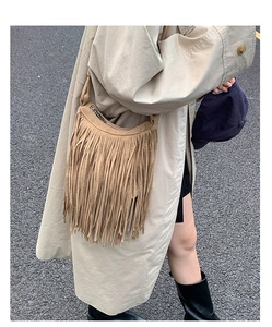 Street style shot of a camel bohemian fringe crossbody bag paired with a beige trench coat