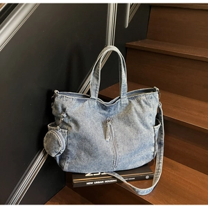 Detail view of washed denim tote bag with side coin pouch and vertical zipper on wooden stairs