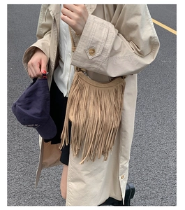 Street style shot of a khaki bohemian crescent bag with long tassels and suede texture