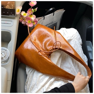 Detailed close-up of a caramel brown faux leather tote bag with glossy finish and ribbon bow