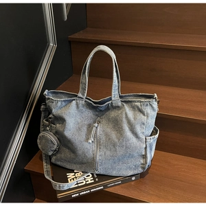 Detail view of denim tote bag with decorative zippers and a small round coin purse charm
