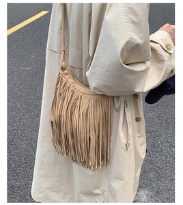 Close-up of bohemian khaki tassel shoulder bag in suede with fringe detail on trench coat