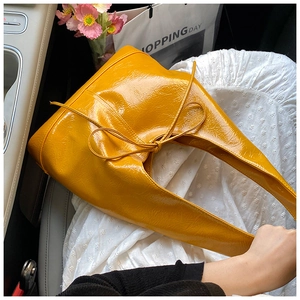 Detail of a bright yellow patent leather tote bag with bow knot in a car setting