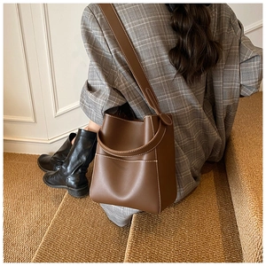Detail of dark brown leather bucket bag with white contrast stitching and wide shoulder strap