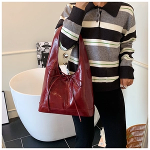 Macro detail of wine red glossy patent leather tote bag featuring a decorative bow knot