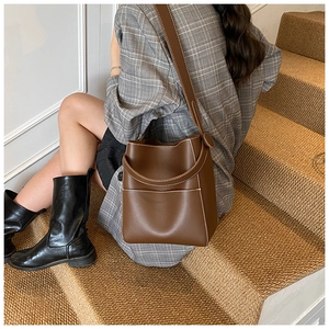 Détail du sac seau en cuir marron foncé avec surpiqûres blanches et large bandoulière