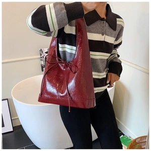 Detail of burgundy patent leather tote bag with glossy finish and elegant bow decoration