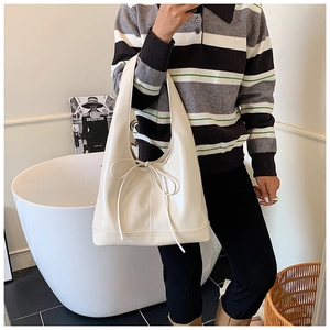 Detail of off-white tote bag with bow accent worn on shoulder in a lifestyle setting