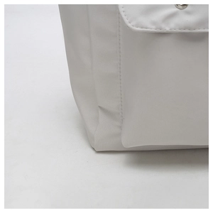 Detail shot of a white canvas tote bag featuring a front pocket with a silver magnetic buckle