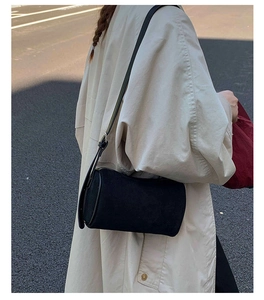 Chic black cylinder crossbody bag in matte finish shown on a model with khaki trench coat