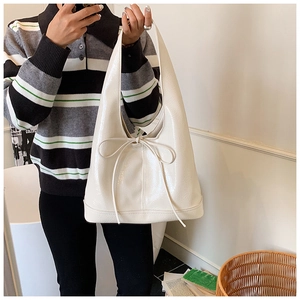 Detailed view of cream patent leather tote bag with a bow detail in a lifestyle setting