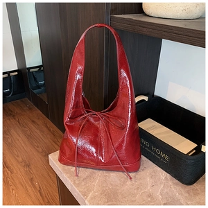 Detail of burgundy patent leather tote bag with glossy finish and ribbon bow accent