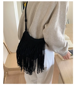 Detail of a black suede crossbody fringe bag shown in a minimalist interior setting