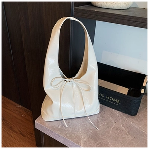 Close-up of a cream white patent leather tote bag featuring a decorative bow tie detail