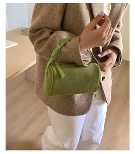 Detailed view of a bright green suede barrel bag featuring a zipper and silver buckle