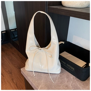Detail shot of a cream white hobo bag featuring a glossy patent finish and a bow tie accent