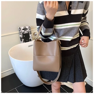 Détail du sac seau en cuir taupe avec coutures contrastées et poignée courte élégante