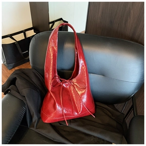 Detailed view of red patent leather shoulder bag with decorative bow and hobo style