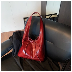 Detail of a deep red patent leather shoulder bag featuring a sleek bow tied on the side