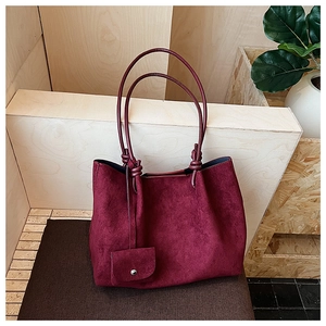 Macro shot of burgundy suede tote featuring knotted handles and a matching mini pouch charm