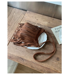 Detailed macro view of brown suede fringe bag with bohemian tassels on wooden table