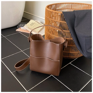 Gros plan détaillé du sac seau en cuir mat marron avec surpiqûres blanches