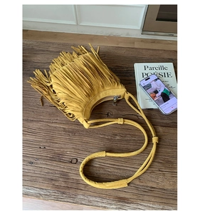 Detail view of yellow suede fringe crossbody bag with boho tassels on wood background