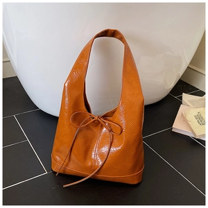 Close-up of brown glossy tote bag featuring crinkled texture and delicate bow detail