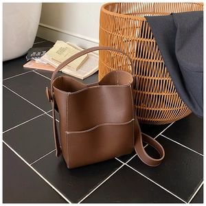 Détail d'un sac seau en cuir marron foncé avec surpiqûres blanches et bandoulière réglable