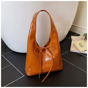 Close-up of a glossy orange patent leather tote bag featuring a decorative bow detail