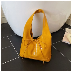 Close-up of bright yellow patent leather tote bag with bow detail and glossy texture