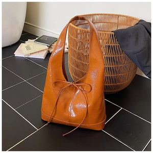 Detail of vintage orange patent leather hobo bag with ribbon bow and glossy crinkled texture