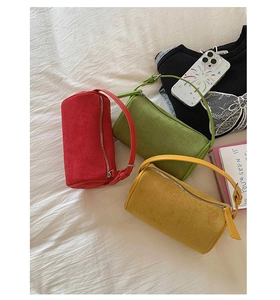 Close-up of matte textured cylinder handbags in red, green, and yellow on a white backdrop