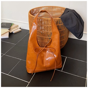 Detailed close-up of glossy caramel orange tote bag with decorative bow and ribbon detail