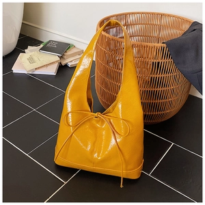 Detail of glossy yellow tote bag with a chic bow accent and spacious patent leather finish