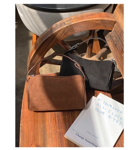 Close-up of suede cylinder bags in coffee brown and black on a wooden chair with sunlight