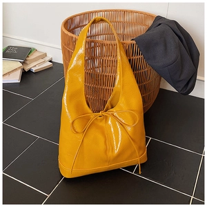 Detail of glossy yellow tote bag showing shiny patent leather texture and bow accent