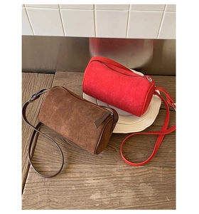 Detail of cylindrical suede shoulder bags in red and brown with metal zipper on wood surface