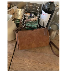 Detail of brown suede barrel bag with contrast leather trim on a dark wooden table