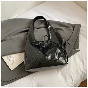 Detail of minimalist black patent leather tote bag with ribbon tie on a grey blazer