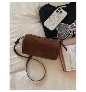 Detail view of the brown cylindrical suede shoulder bag with silver zipper and strap
