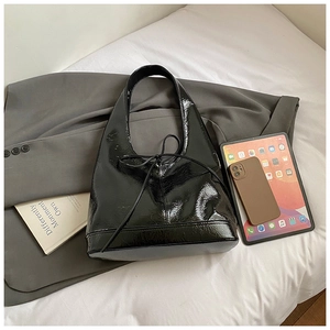 Detail of black glossy leather hobo bag with ribbon bow and crinkled texture