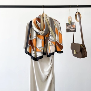 Close-up of geometric silk scarf in orange and grey paired with a beige dress