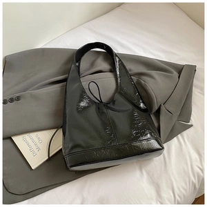 Detail of glossy black patent leather shoulder bag with wide strap on a grey suit jacket