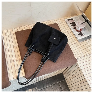 Close-up of black matte suede tote bag featuring sleek knotted handles and matching small pouch