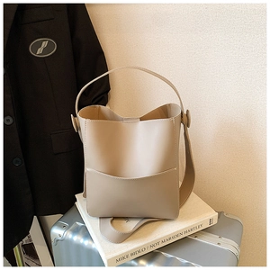 Sac seau beige chic avec bandoulière à côté d'une valise pour voyage et trajet