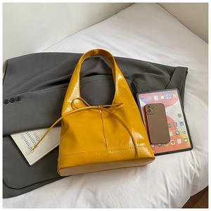 Detailed macro view of the yellow patent leather surface and bow knot on the tote bag