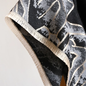 Detail of cashmere style scarf featuring black and gold jacquard mountain pattern and fringe