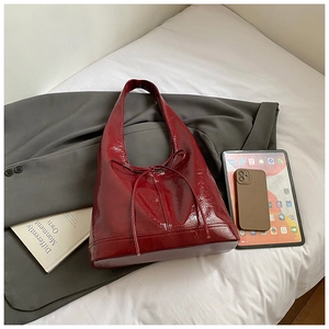 Detailed view of burgundy glossy leather tote bag with thin ribbon decoration on grey blazer
